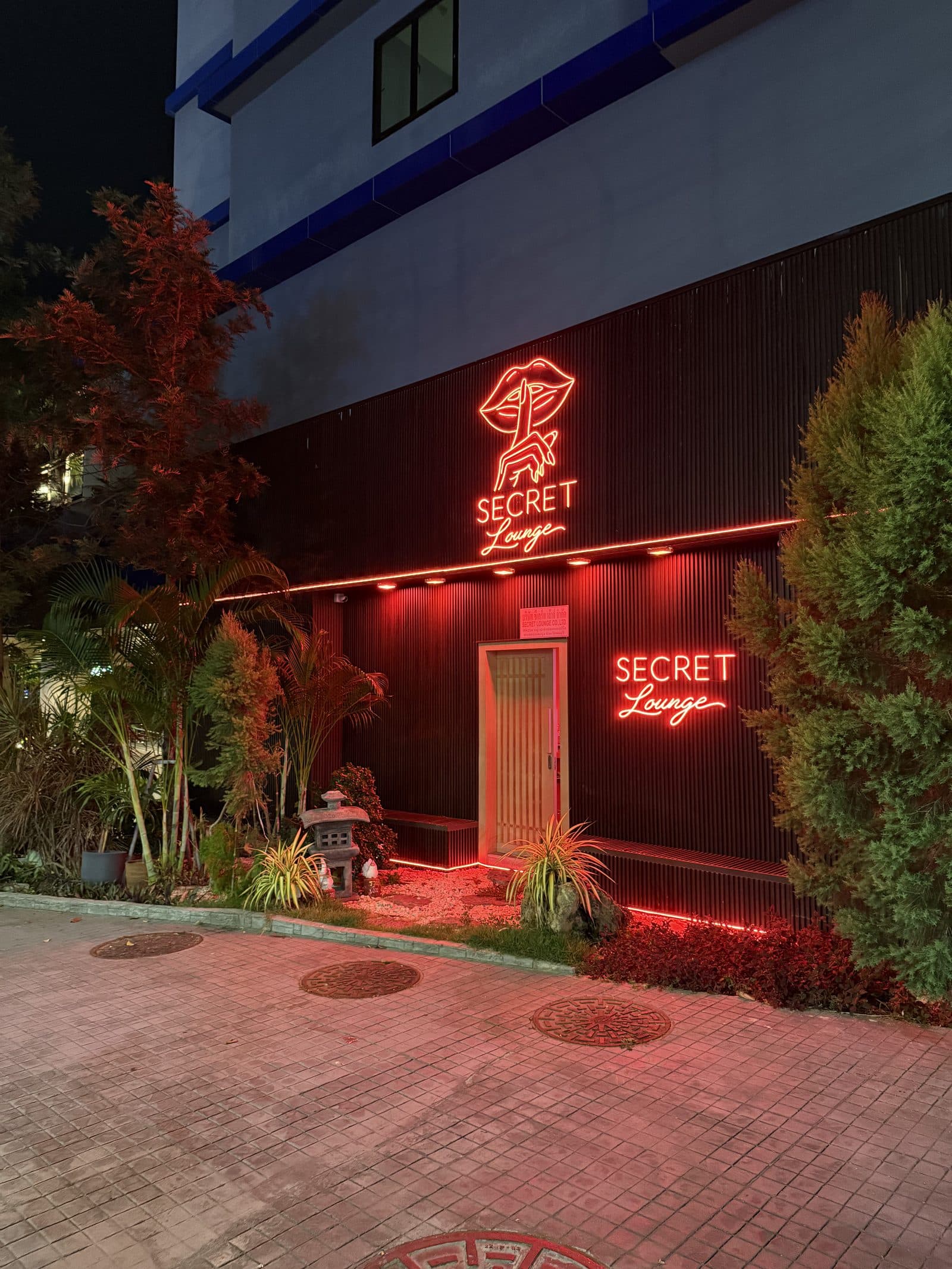 Secret Lounge red neon facade at night — black slatted wall, zen garden and hidden wooden door, Pattaya